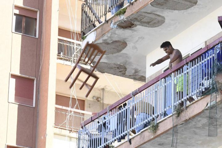 Un residente del palazzo isolato lancia una sedia dal balcone (Ansa)
