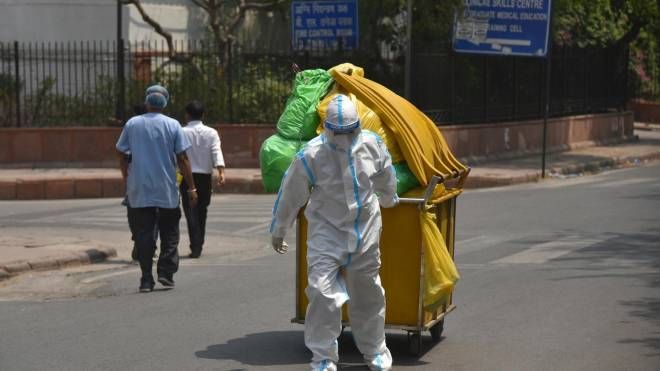 Operatore sanitario trasporta rifiuti Covid-19 al di fuori dell'obitorio dell'ospedale a New Delhi (Ansa)