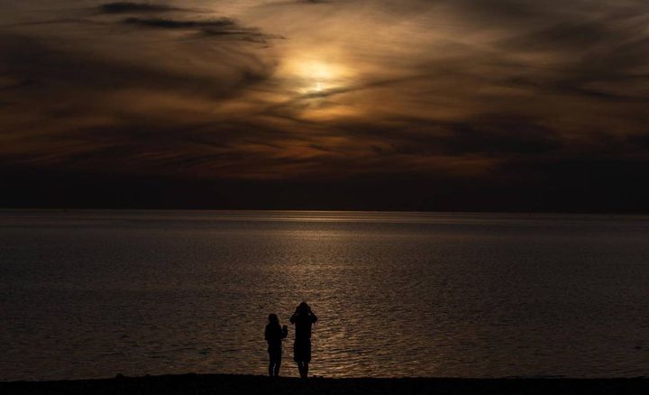 Persone in riva al mare guardano l'eclissi (Ansa)