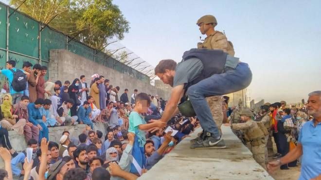 Il console italiano a Kabul Tommaso Claudi aiuta un bambino spaventato a superare il muro dell'aeroporto (Ansa)