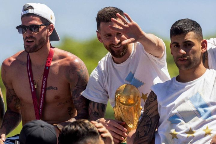 Messi saluta la folla con la Coppa del mondo. Insieme a lui De Paul e Romero