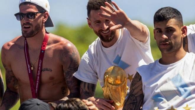 Messi saluta la folla con la Coppa del mondo. Insieme a lui De Paul e Romero