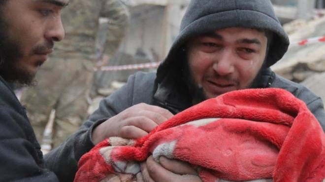 A Jandaris siriano piange mentre tiene in braccio il figlio estratto dalle macerie (Ansa)